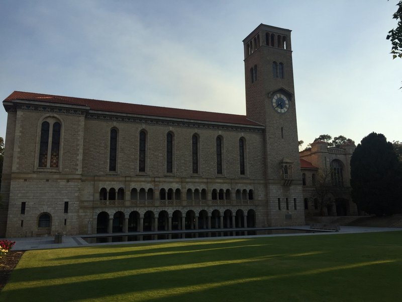 西澳大学校园风景：古老砂岩建筑与现代设施融合，前方草坪开阔，天空湛蓝